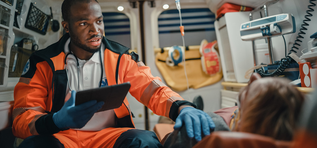 Emergency Medical Technician assisting a patient in the back of an ambulance.