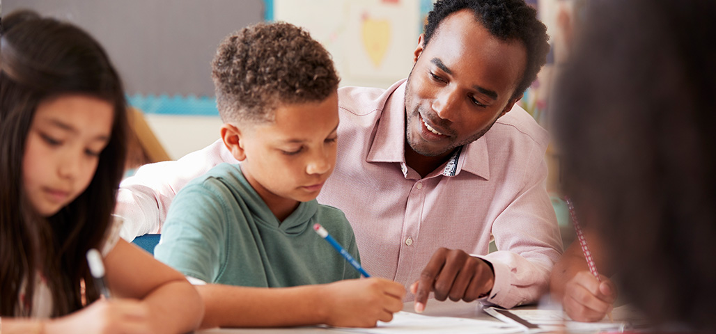 A man helping a child with schoolwork in a classroom.