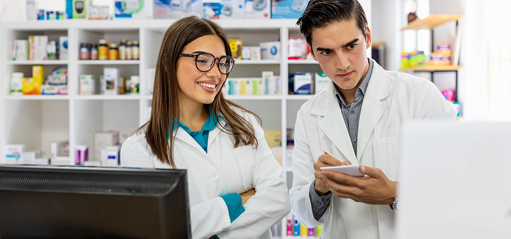 Two people in lab coats writing down results from a computer.