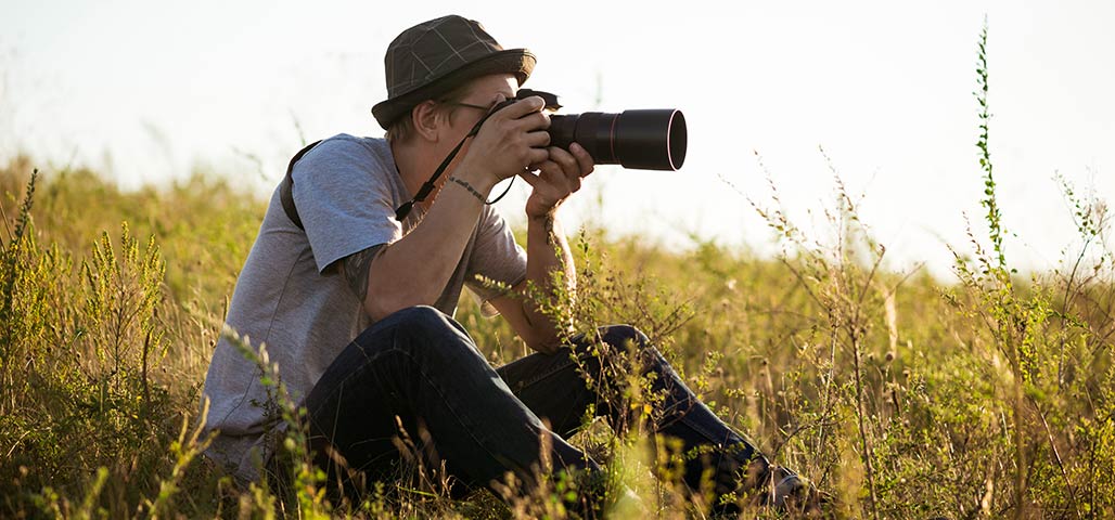 Man outdoors in a field of grass holding camera while taking a picture.